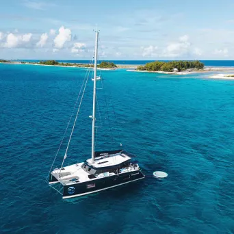 Sailboat in clear blue water near small island, under a sunny sky.