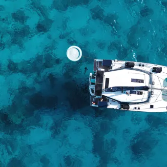 Aerial view of a sailboat on clear blue water with a circular float nearby.