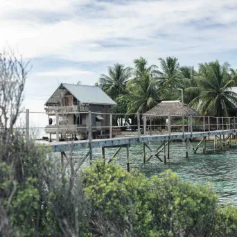 Wooden huts on stilts over water, surrounded by palm trees.