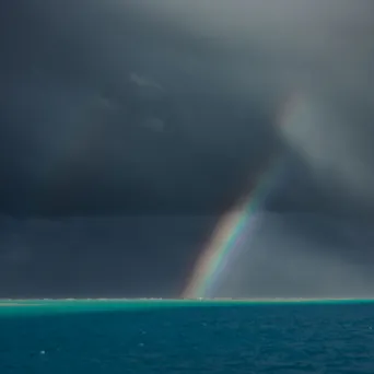 Rainbow over dark sea and sky, with sunlight breaking through clouds.