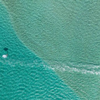 Aerial view of a kite surfer in turquoise water with another kite nearby.
