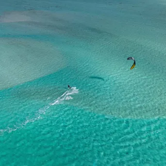 Person kiteboarding on clear turquoise water under a blue sky.