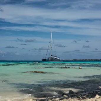 Sailboat anchored in turquoise waters near rocky shore under cloudy sky.