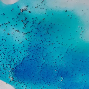 Aerial view of a bright blue ocean with scattered dark patches.