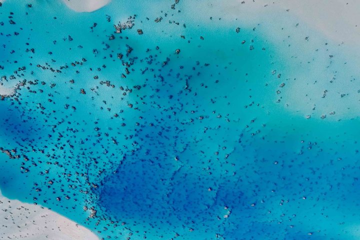 Aerial view of a bright blue ocean with scattered dark patches.
