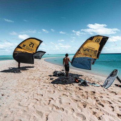 Two people on a sandy beach carrying kites near the ocean.