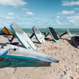Surfboards and sails on a sandy beach with blue skies and ocean.