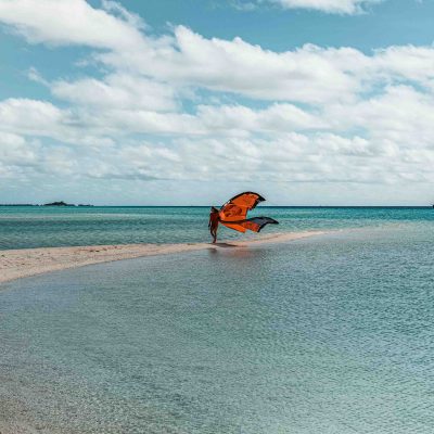 Person with orange wings on beach near ocean under cloudy sky.