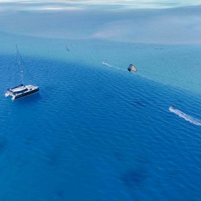 Aerial view of a yacht and kite surfers on a clear blue sea.