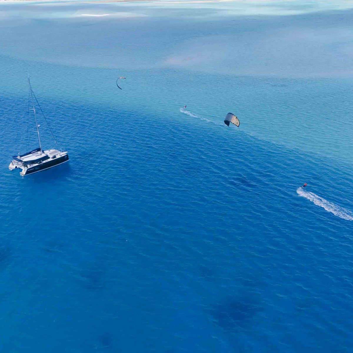 Aerial view of a yacht and kite surfers on a clear blue sea.