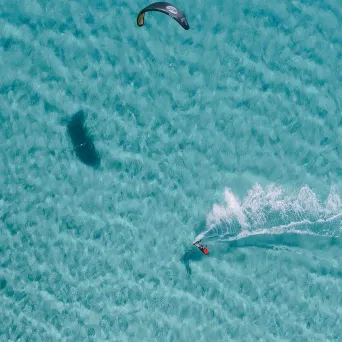 Overhead view of a person kiteboarding on clear turquoise water.