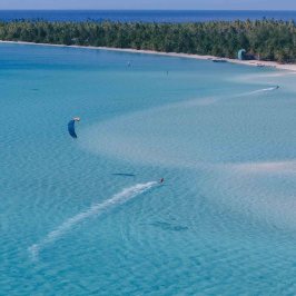 Person kite surfing on clear blue water near a tropical island.