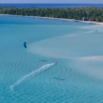 Person kite surfing on clear blue water near a tropical island.