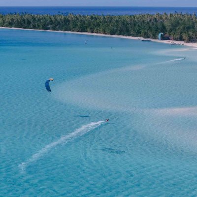 Person kite surfing on clear blue water near a tropical island.