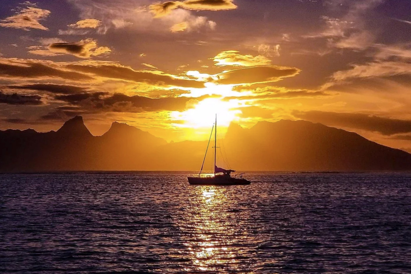Sailboat on the sea at sunset with mountains in the background.