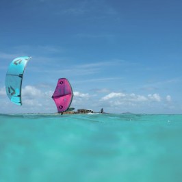 Two kite surfers on turquoise water under clear blue sky.