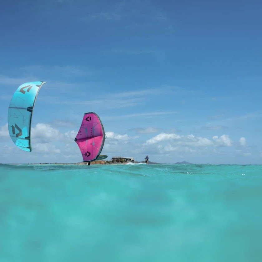 Two kite surfers on turquoise water under clear blue sky.