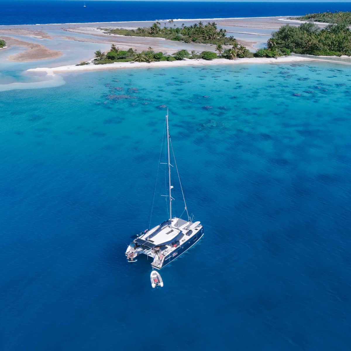 Sailboat anchored in clear turquoise water near a tropical island.