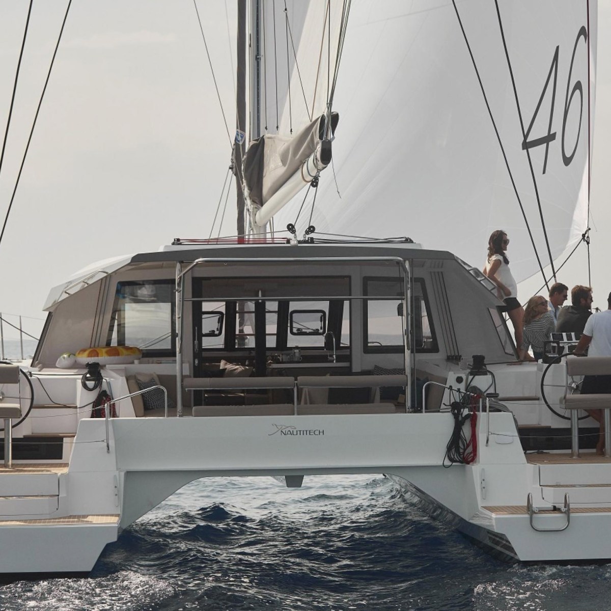 Catamaran sailing with group on deck, view from rear.