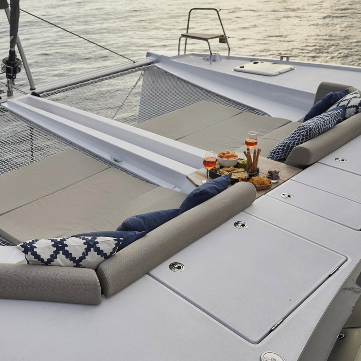 Luxury yacht deck with cushioned seating and drinks, overlooking the ocean.