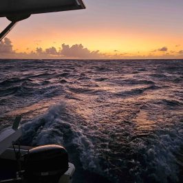 Ocean view from a boat at sunset with choppy waves and an orange sky.
