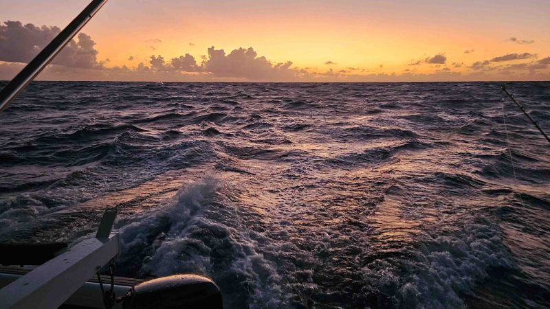 Ocean view from a boat at sunset with choppy waves and an orange sky.