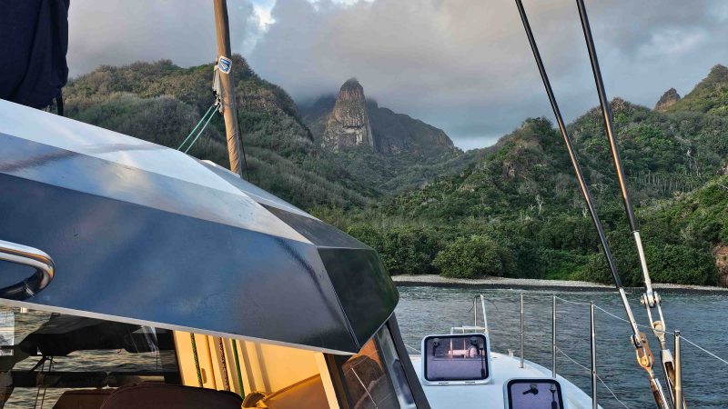 Sailboat in front of lush, mountainous landscape under a cloudy sky.