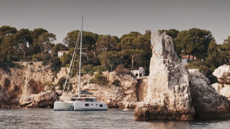 Catamaran near rocky coastline with trees and cliffs.