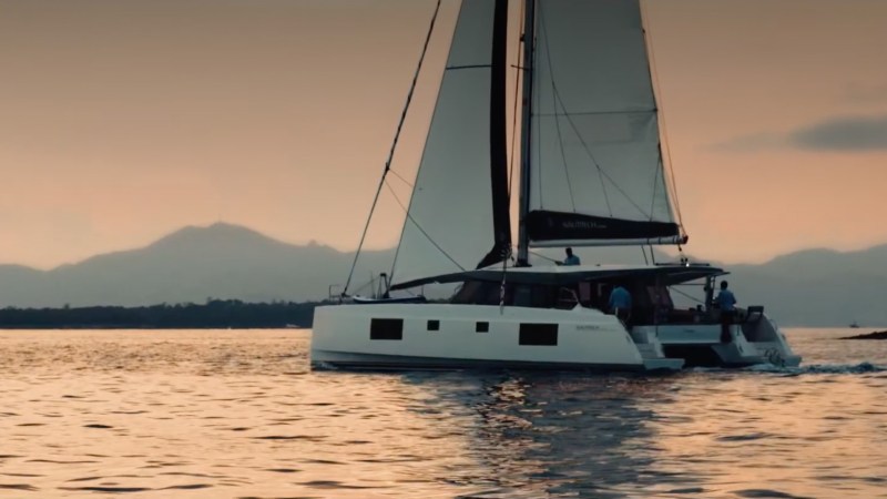 Sailboat on calm water at sunset with distant mountains.