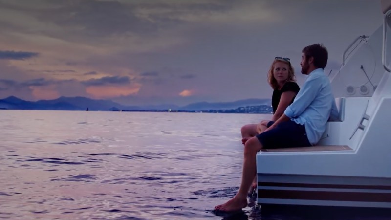 Two people sitting on a boat at sunset, looking at each other.