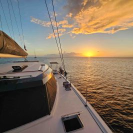 Sailboat at sunset with orange clouds and calm sea.