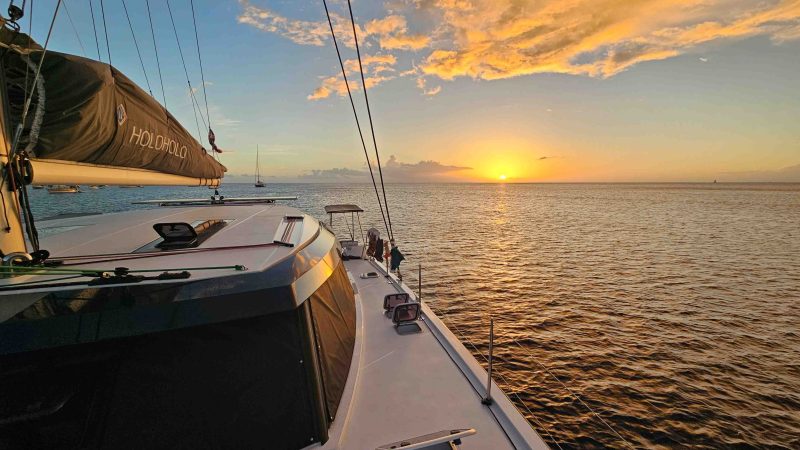 Sailboat at sunset with orange clouds and calm sea.