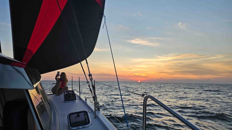Sailboat on ocean at sunset with people on deck.
