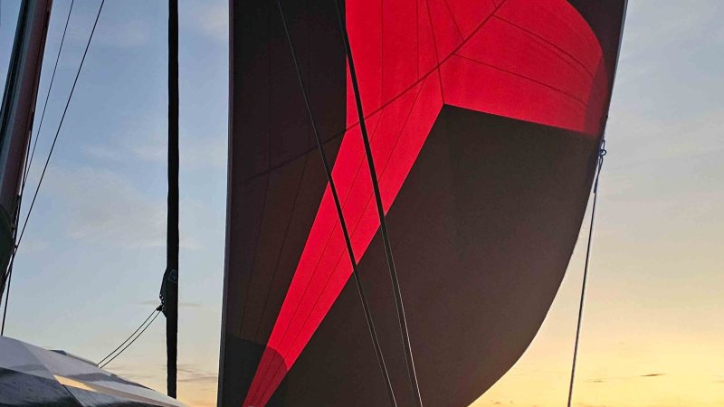 Sailboat with black and red sail at sunset over the ocean.