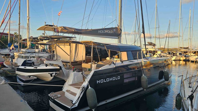 Marina with a large, sleek catamaran named Holo Holo docked beside smaller boats.