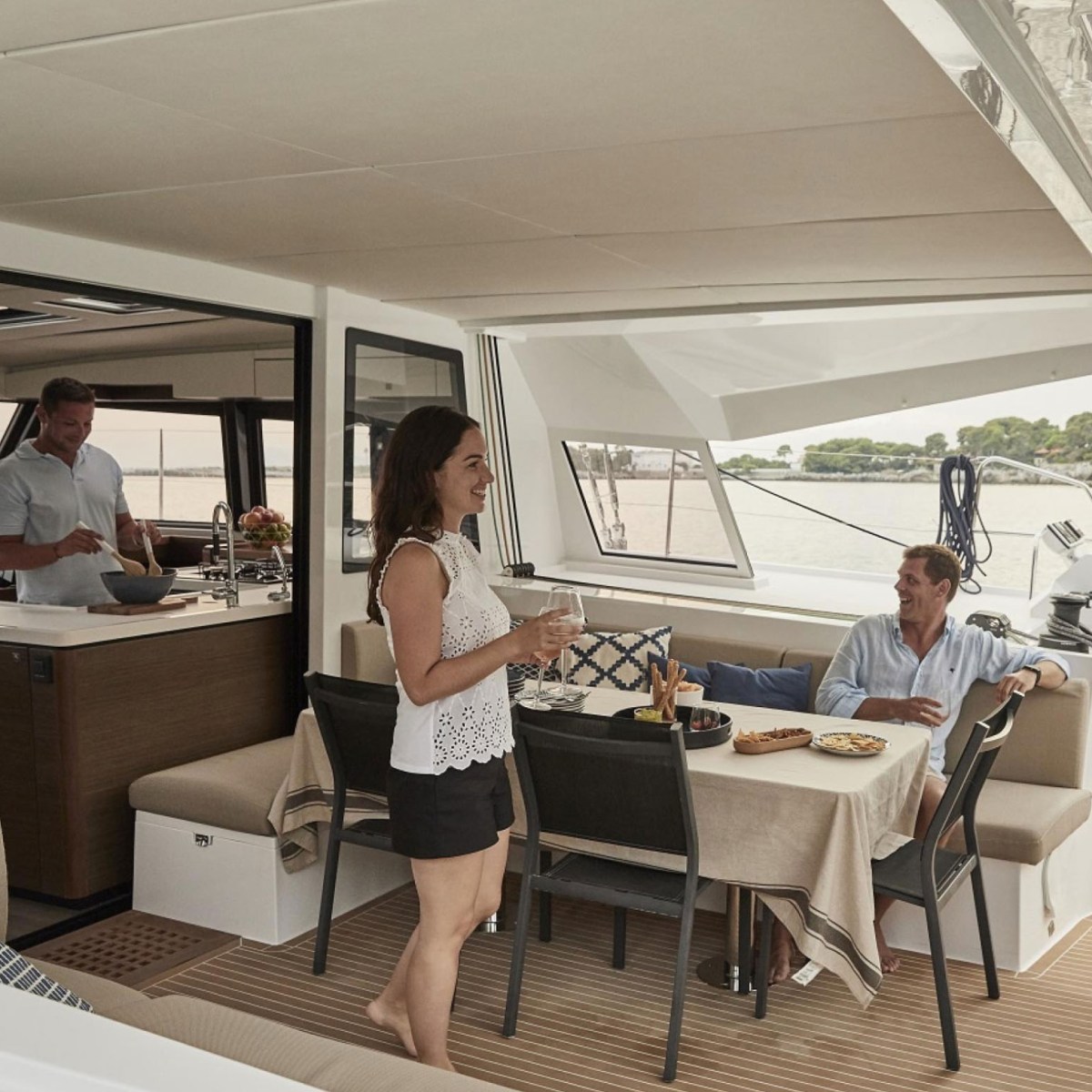 People relaxing and dining on a yacht's deck with a kitchen area.