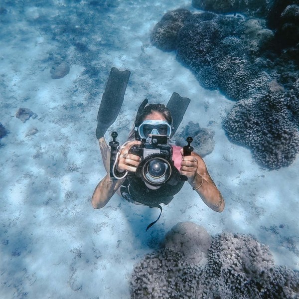 Diver underwater holding a camera near coral reef.