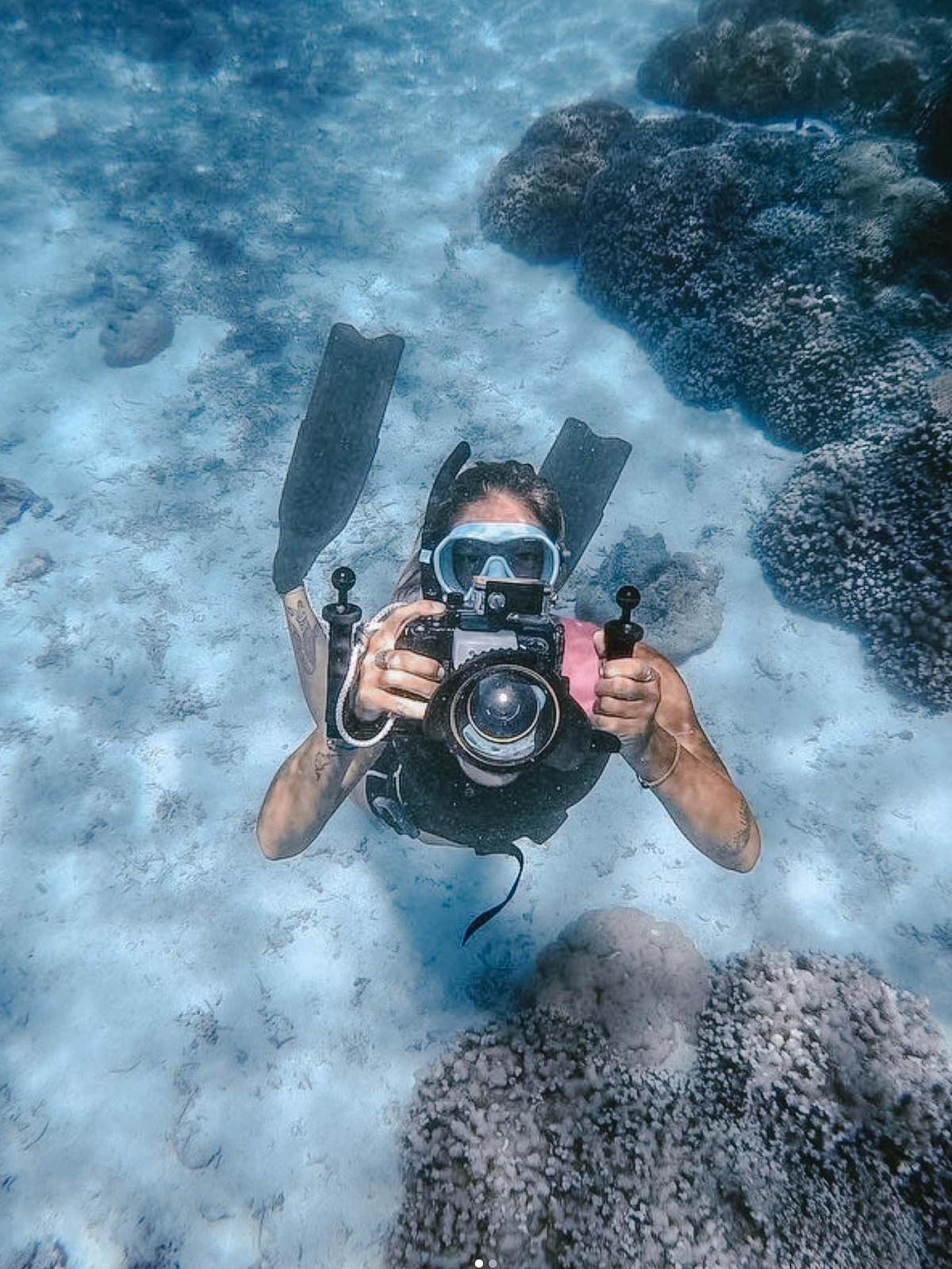 Diver underwater holding a camera near coral reef.