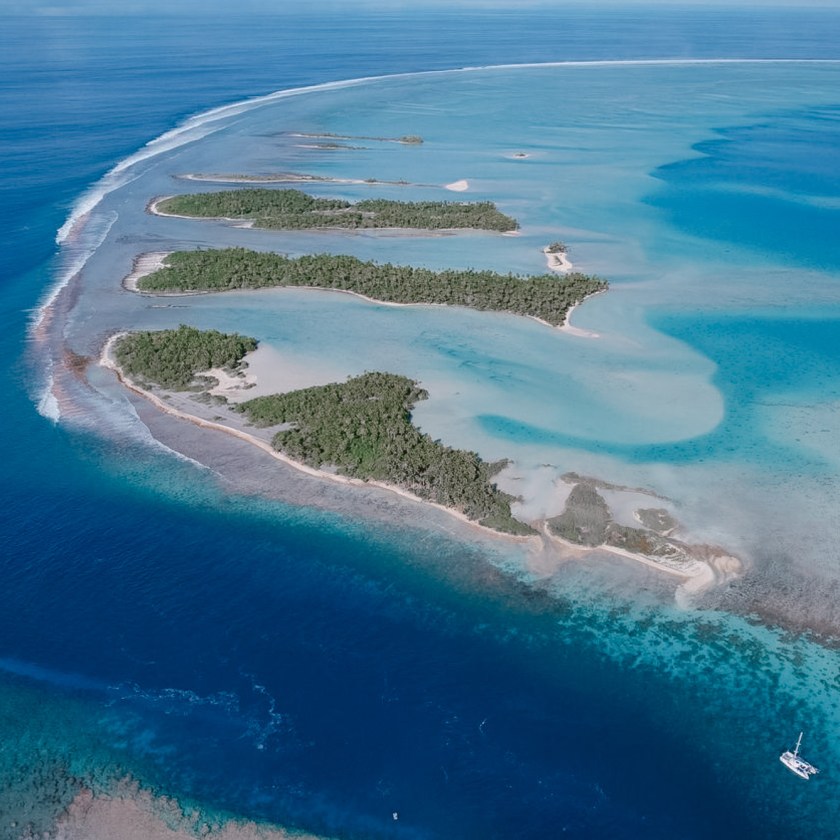 Aerial view of tropical islands surrounded by turquoise water and coral reefs, with a small boat on the right.