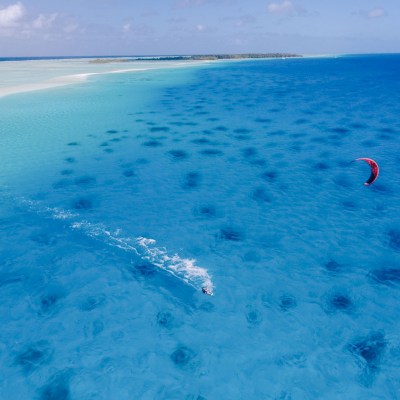 Aerial view of a person kiteboarding on crystal-clear turquoise water.