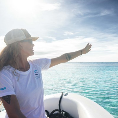 Person in a boat pointing towards the ocean on a sunny day.
