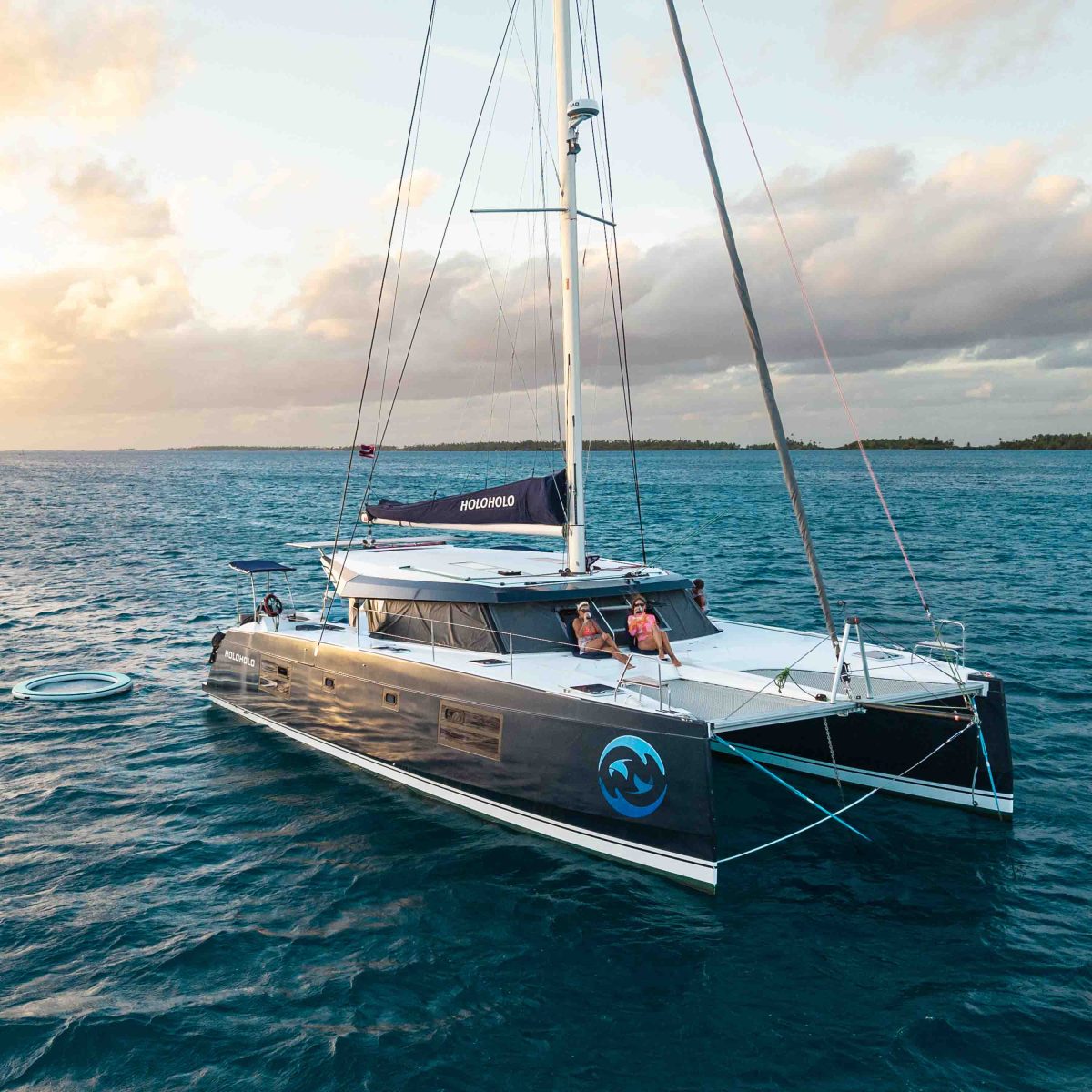 Catamaran sailing on the ocean with people relaxing on deck.