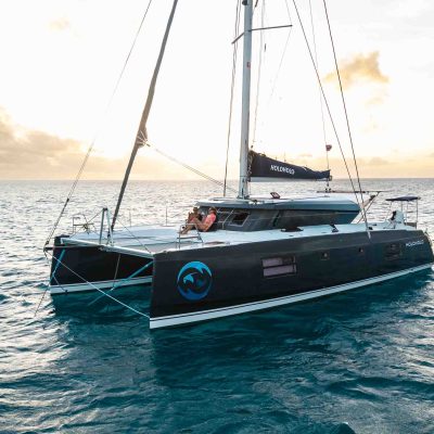 Sailboat with black hull on calm ocean during sunset.