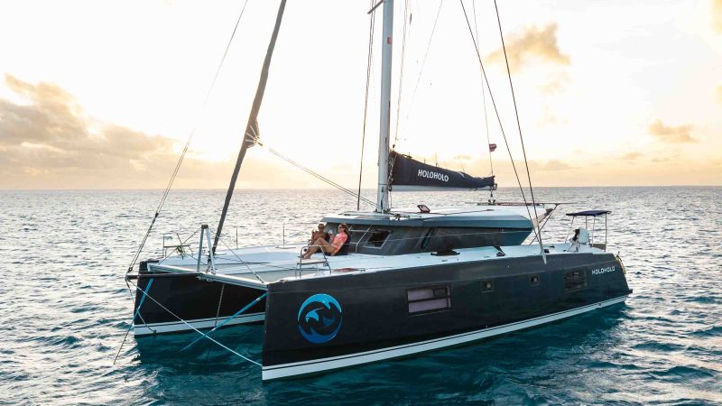 Sailing catamaran with people on deck at sunset on the ocean.