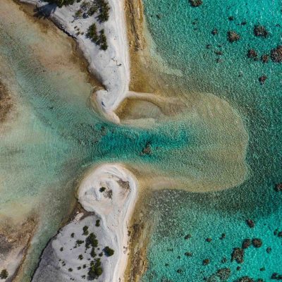 Aerial view of sandy beach with turquoise water and rocky formations.