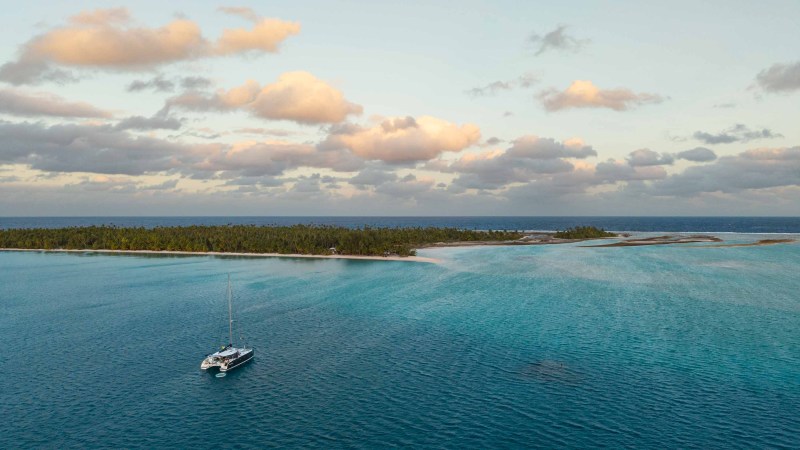Aerial view of boat on calm sea near lush island under cloudy sky.