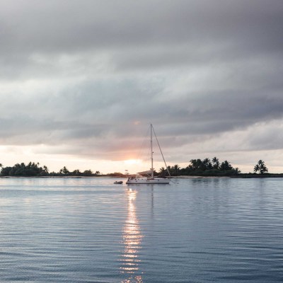 A sailboat on calm water at sunset with cloudy skies.