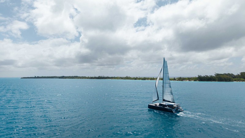 A sailboat on a vast blue ocean with a cloudy sky and distant shoreline.