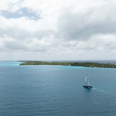 Sailboat on blue ocean near tropical island with cloudy sky.
