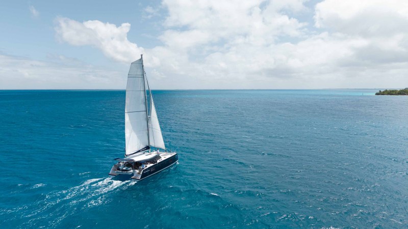 Catamaran sailing on open blue sea under a partly cloudy sky.